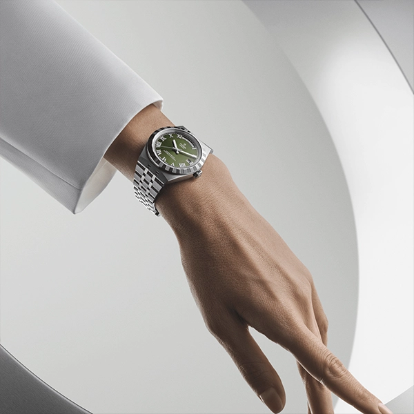 Silver stainless steel luxury wristwatch with green dial on model's wrist against minimalist white background