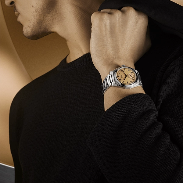Close-up of man wearing stainless steel luxury wristwatch with champagne dial and metal bracelet, black sweater.