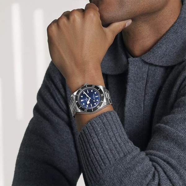 Close-up of wrist wearing stainless steel dive watch with blue dial and bracelet, model in gray sweater