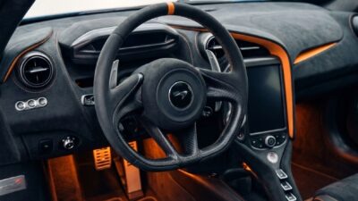 Luxury sports car interior with carbon-fiber steering wheel, Alcantara seats, orange ambient lighting, touchscreen.