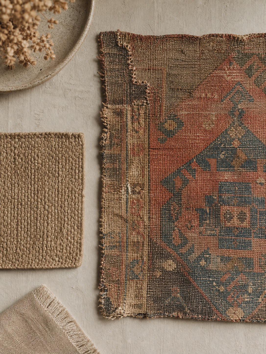 Vintage and new bohemian materials flat lay An overhead flat lay comparing a plain new jute swatch with a worn antique kilim fragment showing patina and repair stitching. | Sky Rye Design An overhead flat lay comparing a plain new jute swatch with a worn antique kilim fragment showing patina and repair stitching.