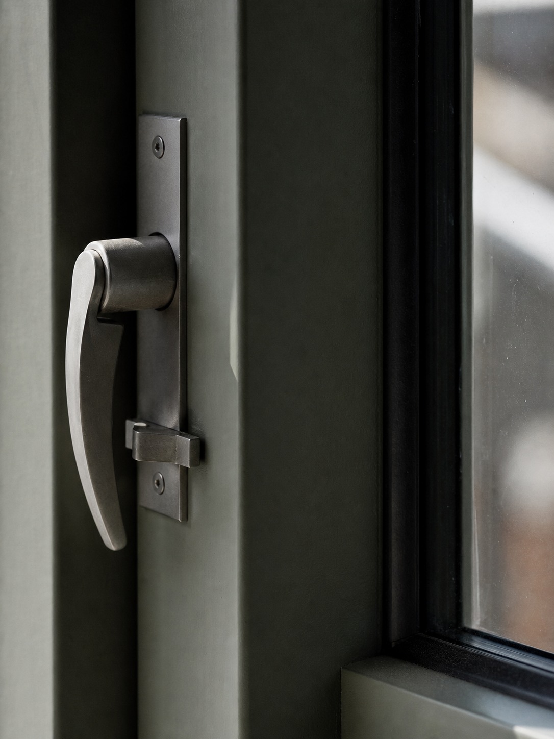 Close still life of a window lock and handle against a matte frame, photographed as a precise architectural detail.