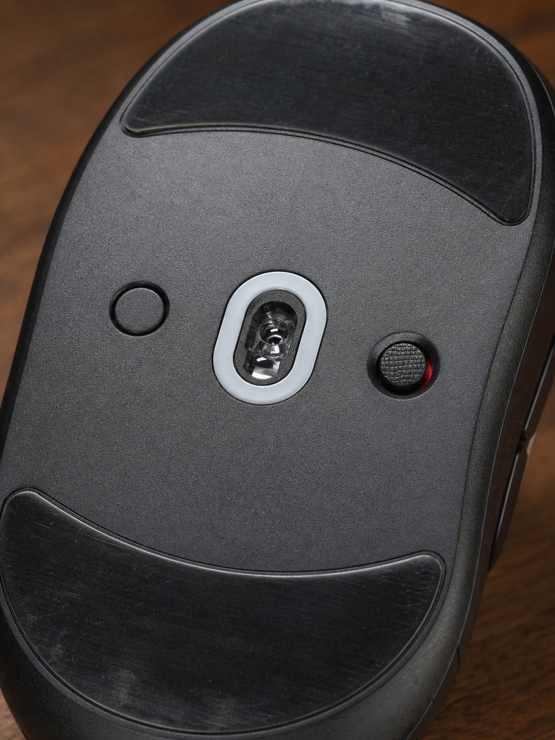 Underside of a wireless gaming mouse showing the sensor lens and glide feet in sharp detail