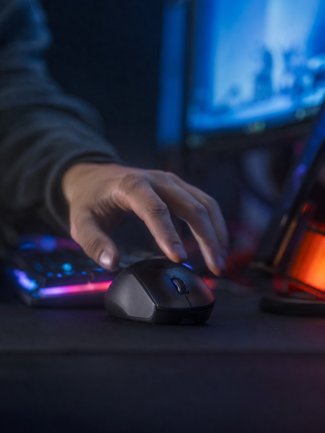 Hand reaching toward a wireless gaming mouse during a gaming session lit by monitor glow