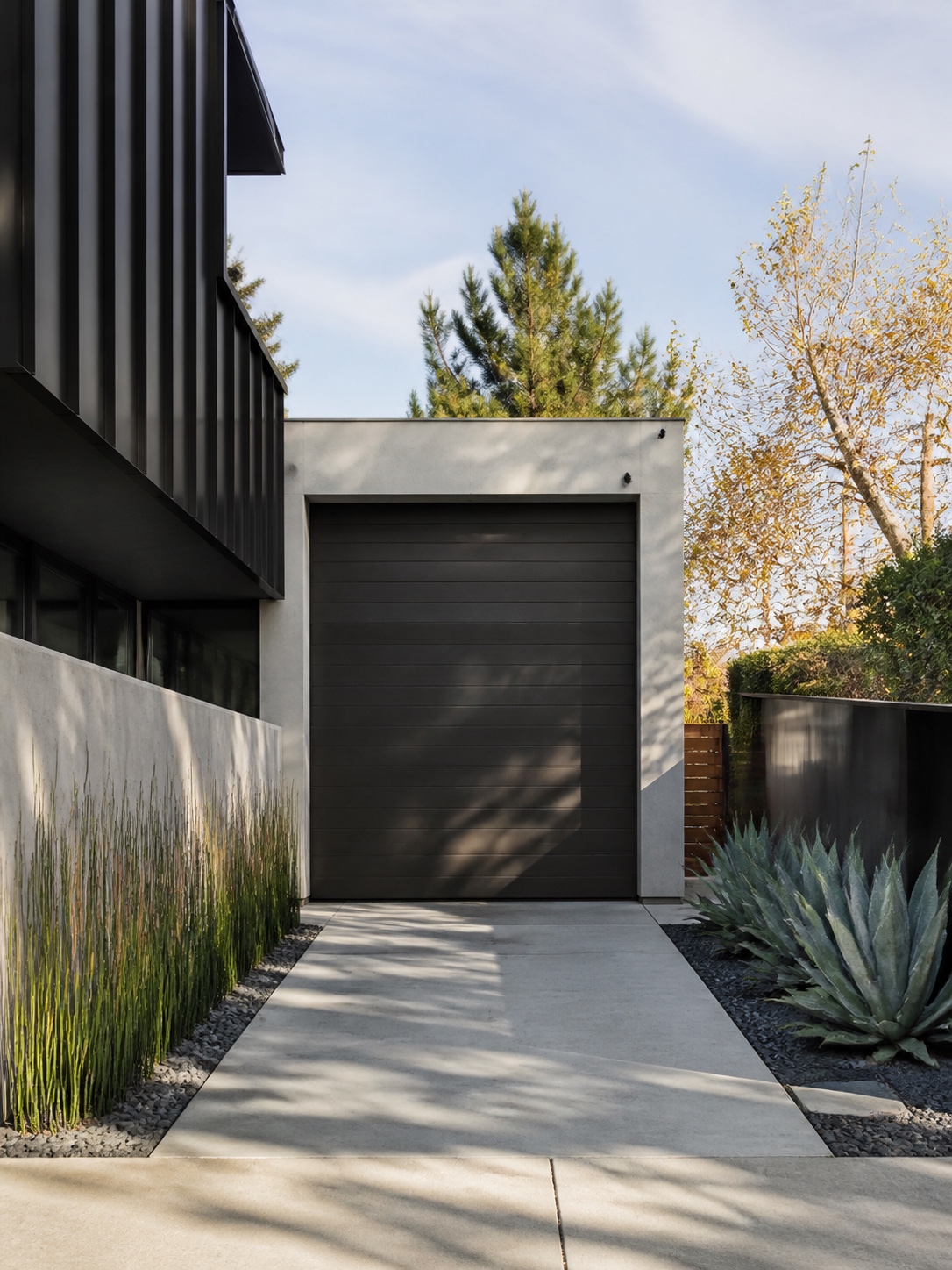 Driveway design idea - Straight driveway for a compact modern lot Front view of a modern home featuring a large dark garage door, white frame, and minimalist drought-tolerant landscaping along a concrete driveway. | Sky Rye Design Straight concrete driveway on a compact modern front yard