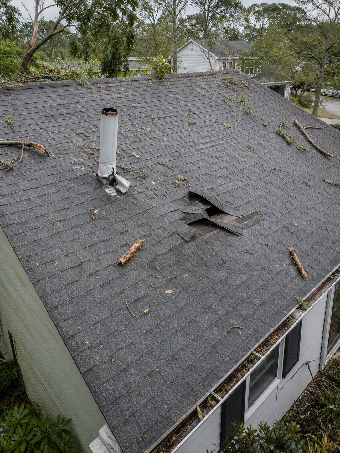 Weathered roof after storm overview Storm-weathered residential roof with debris, lifted shingles, and bent flashing near a vent pipe. | Sky Rye Design Storm-weathered residential roof with debris, lifted shingles, and bent flashing near a vent pipe.