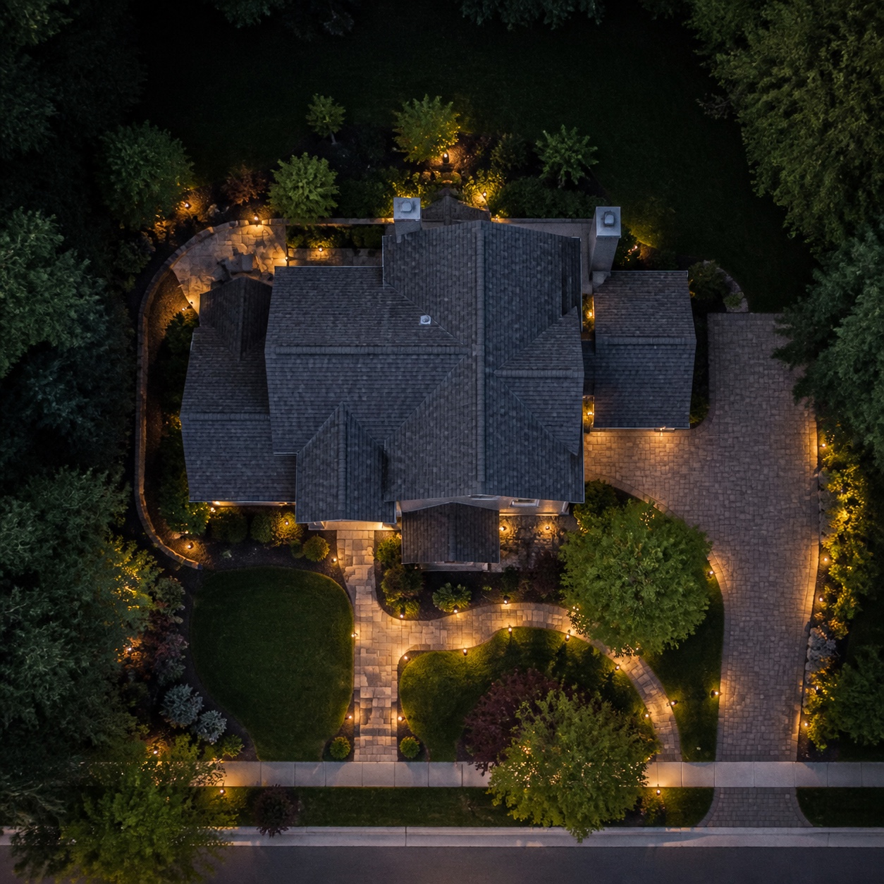 Aerial view of a warmly lit property at dusk Top-down aerial view of a house and front yard with warm entry and path lighting at dusk. | Sky Rye Design Top-down aerial view of a house and front yard with warm entry and path lighting at dusk.