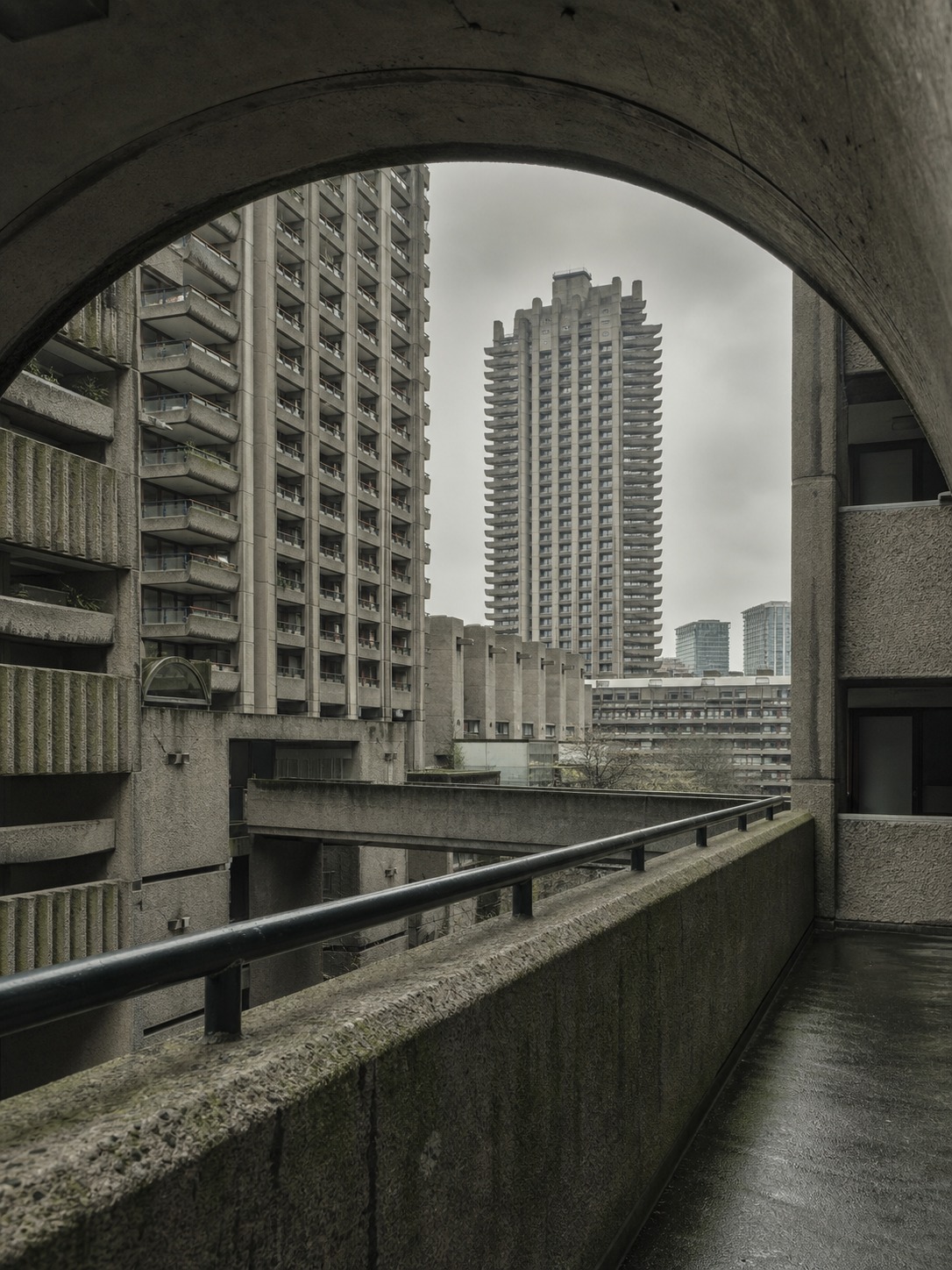 A Barbican-style residential tower cluster framed through a raised concrete walkway.