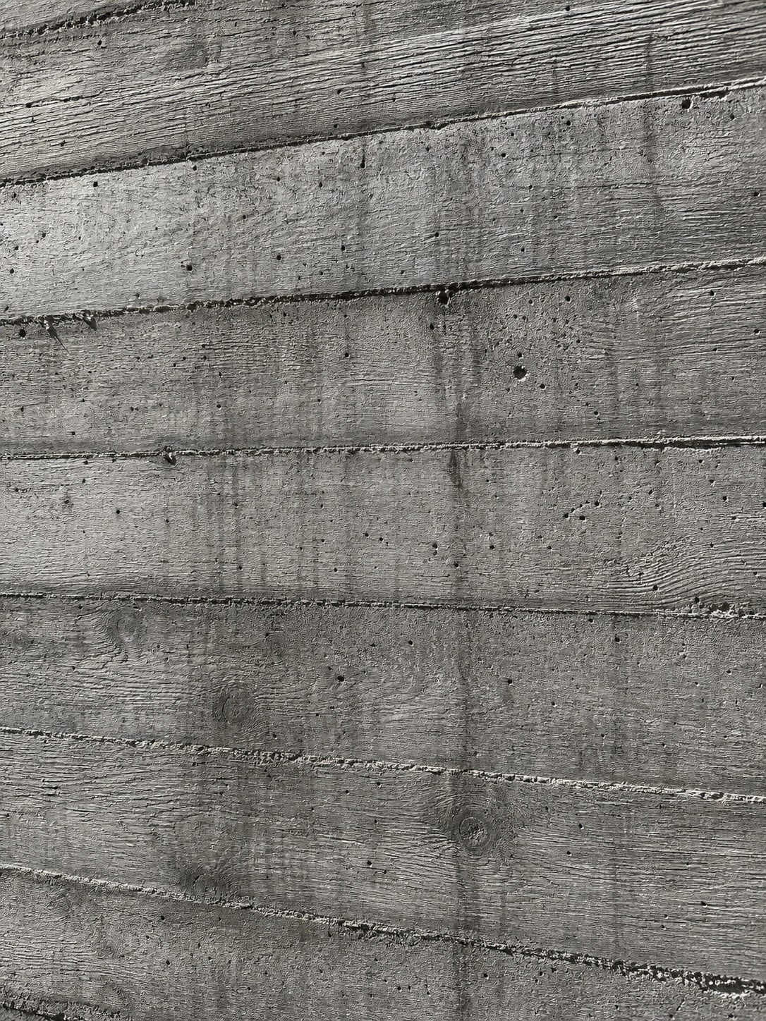 A close detail of a raw board-form concrete wall, with wood-grain impressions and fine aggregate visible.