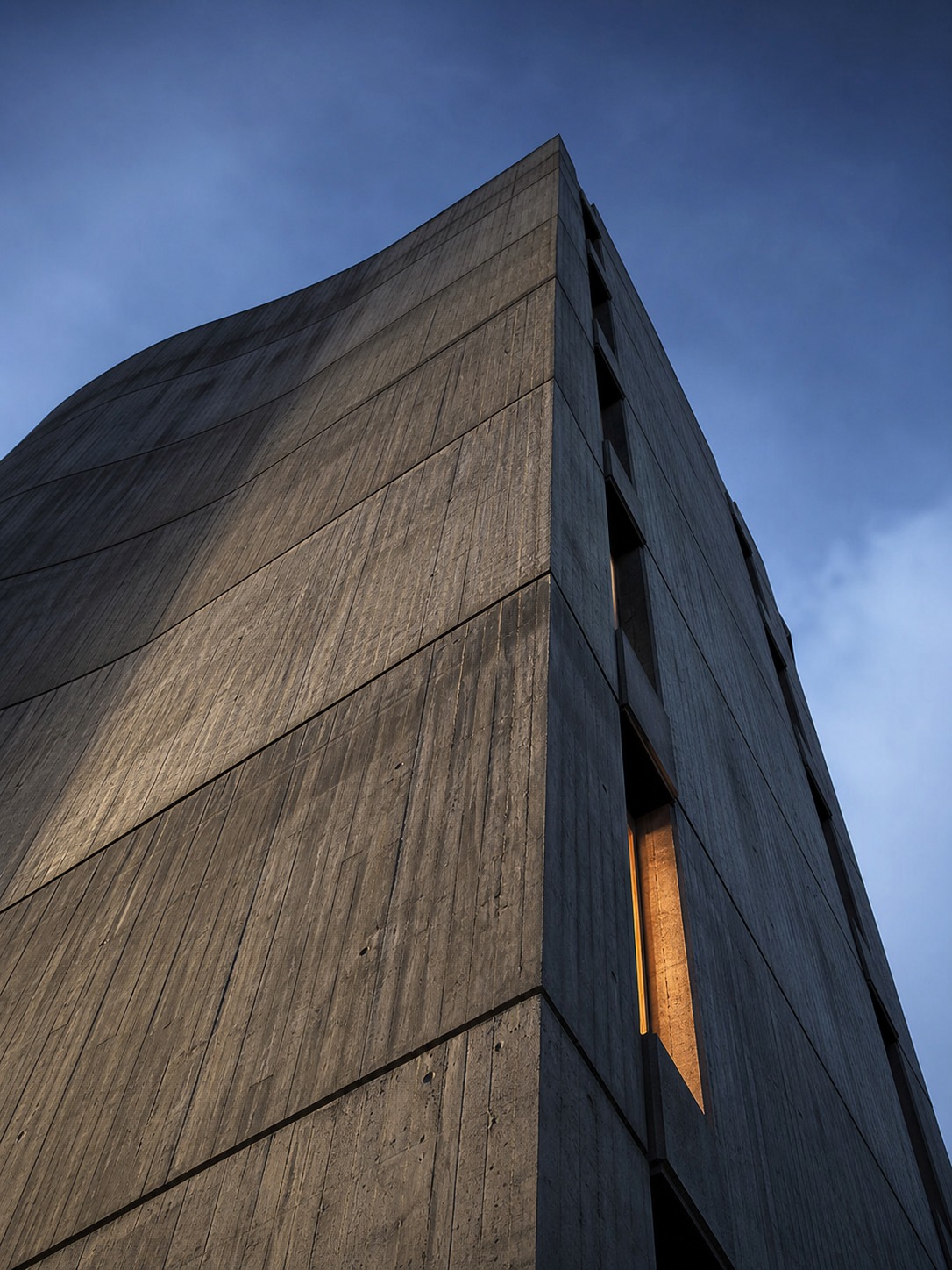 A low-angle view of a brutalist concrete facade at dawn, with board-form texture catching the light.