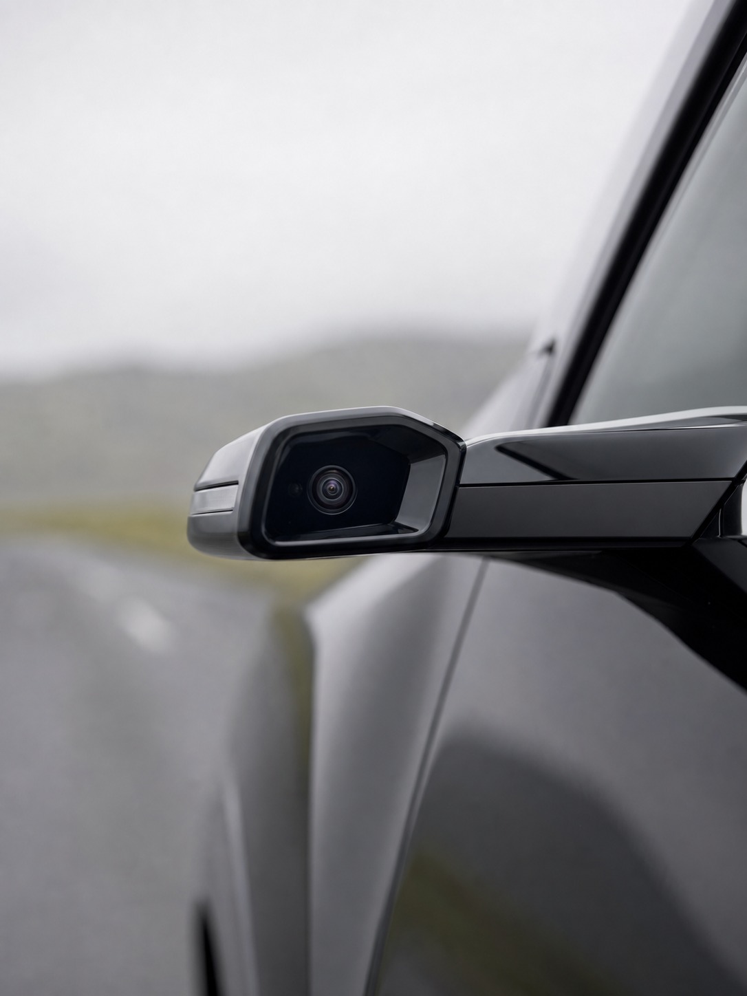 Camera side mirror on a modern EV A sleek camera-based side mirror housing on a modern EV, photographed against a soft road background. | Sky Rye Design A sleek camera-based side mirror housing on a modern EV, photographed against a soft road background.