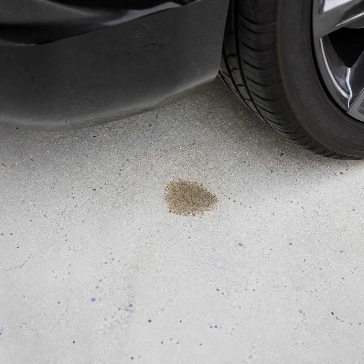 Small fluid stain visible on a light garage floor beneath a parked car.