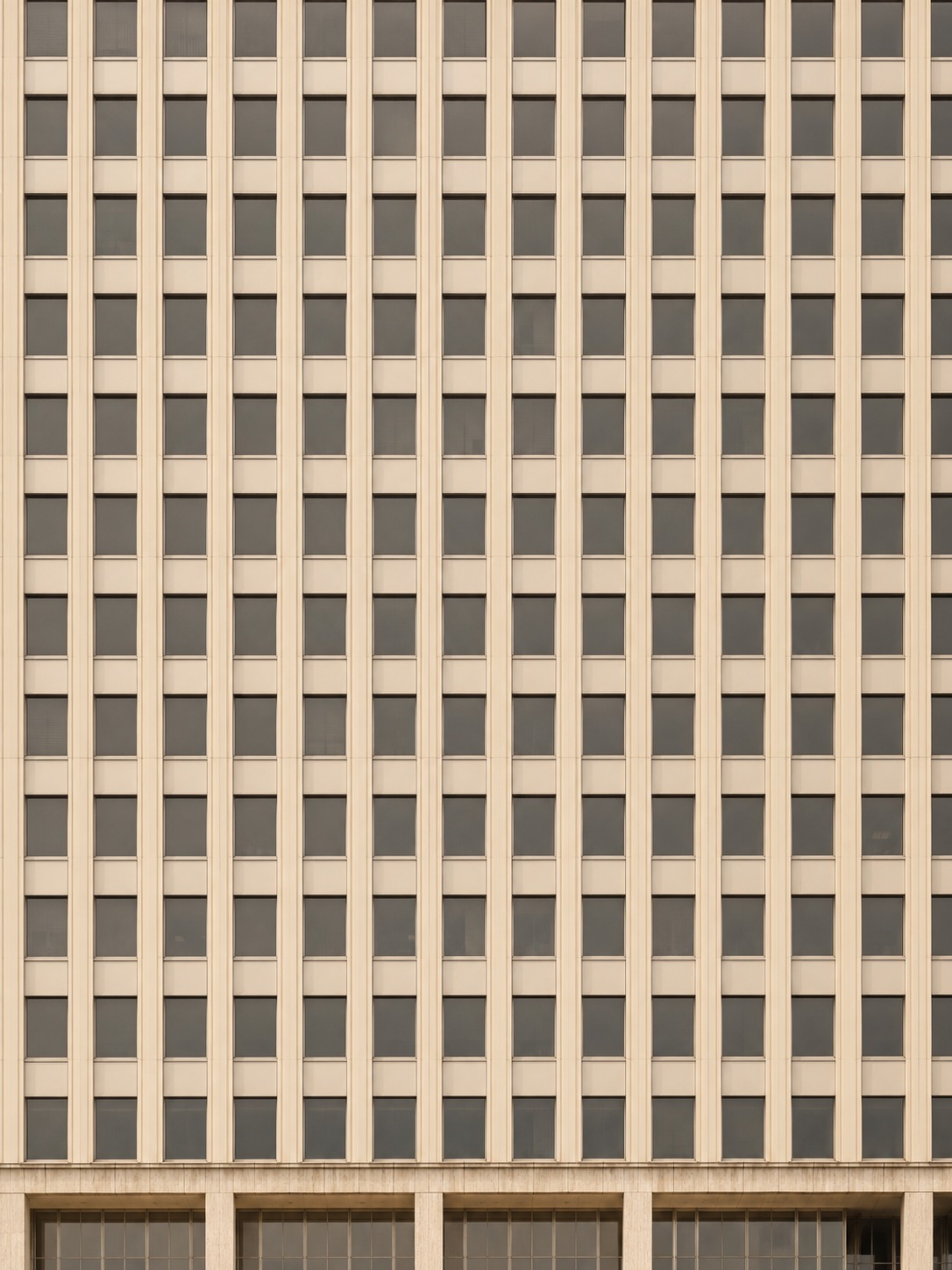 A straight-on formalist office tower facade with vertical spandrels and rows of recessed windows.