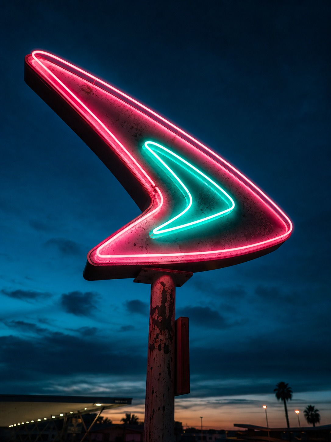 A Googie-style motel sign glowing against a deep dusk sky, with a boomerang silhouette.