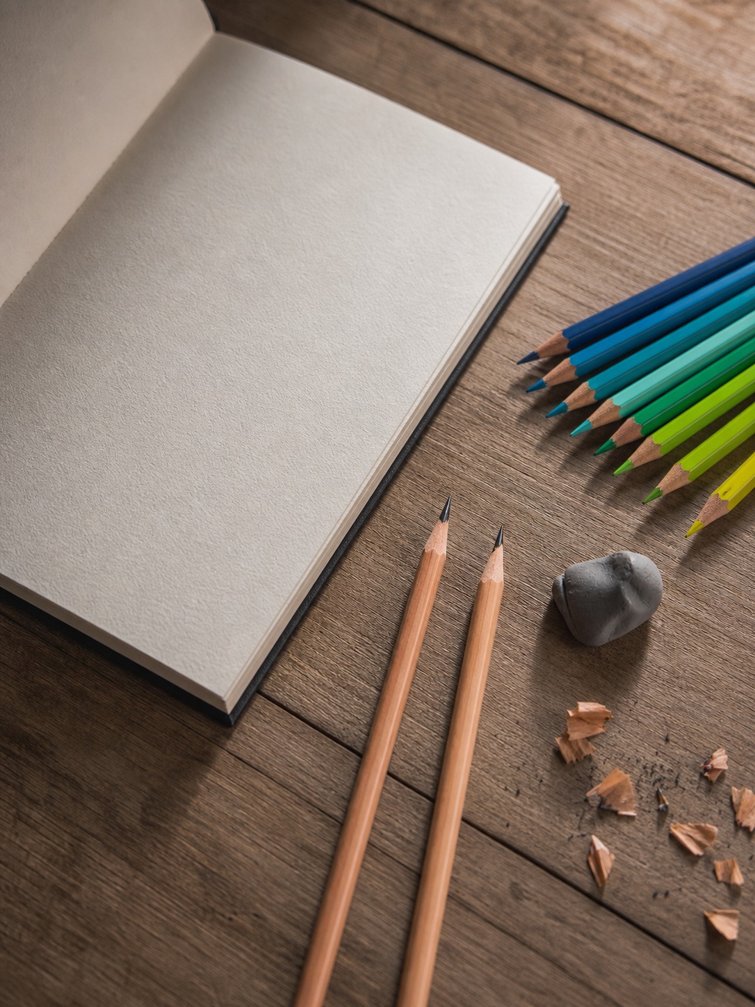 Grass drawing pencils and colored pencil materials Graphite pencils, green colored pencils, kneaded eraser, and open sketchbook arranged on a desk. | Sky Rye Design Graphite pencils, green colored pencils, kneaded eraser, and open sketchbook arranged on a desk.