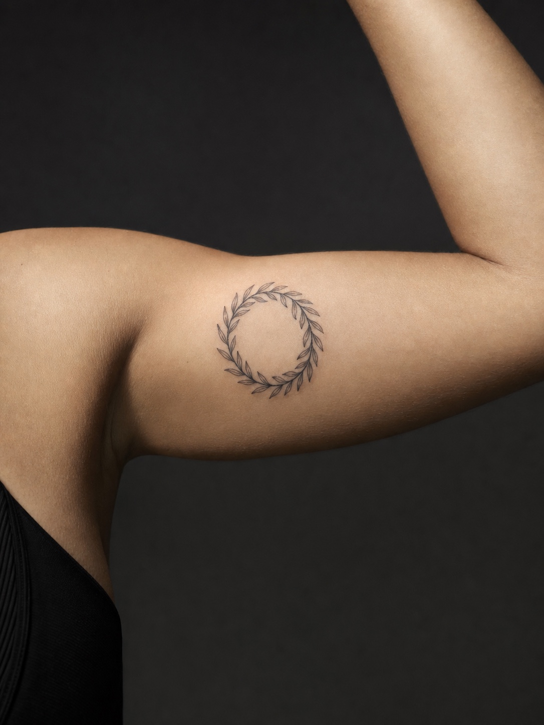 Laurel wreath upper arm Greek tattoo Fine-line laurel wreath tattoo on an upper arm against a dark studio background. | Sky Rye Design Fine-line laurel wreath tattoo on an upper arm against a dark studio background.