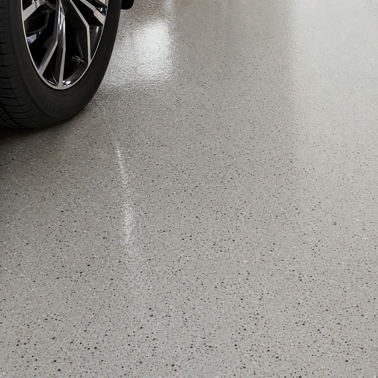 Light epoxy garage floor finish reflecting overhead task lighting near a tire.