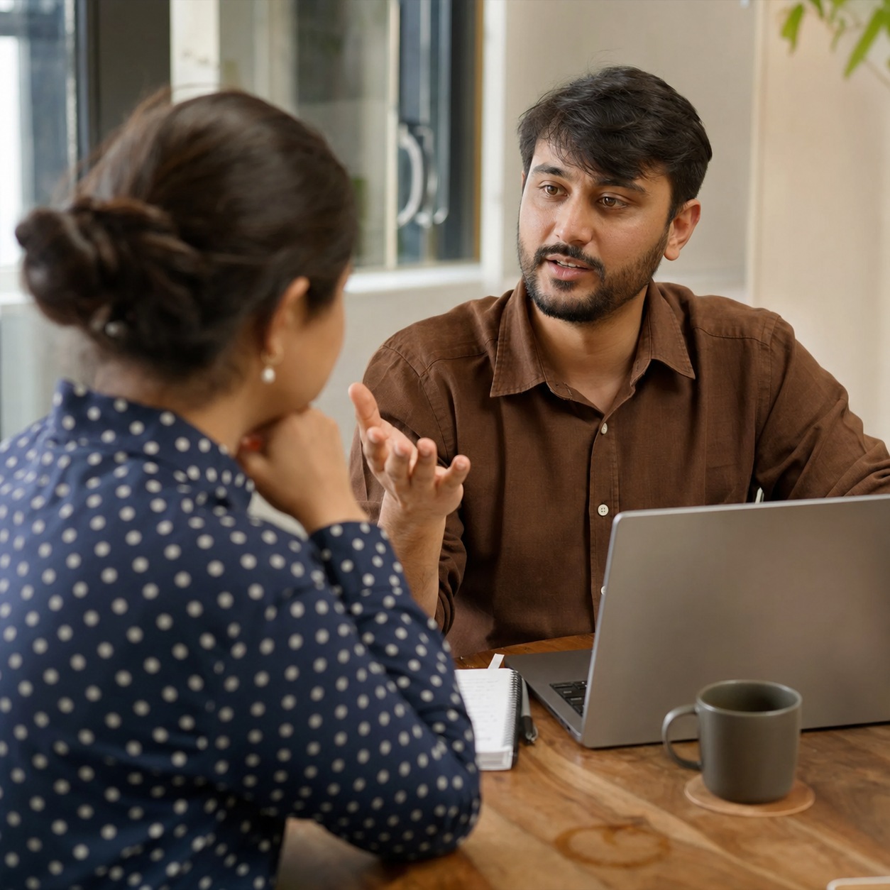 Two people discussing vendor support details at a small meeting table with a laptop and notepad.