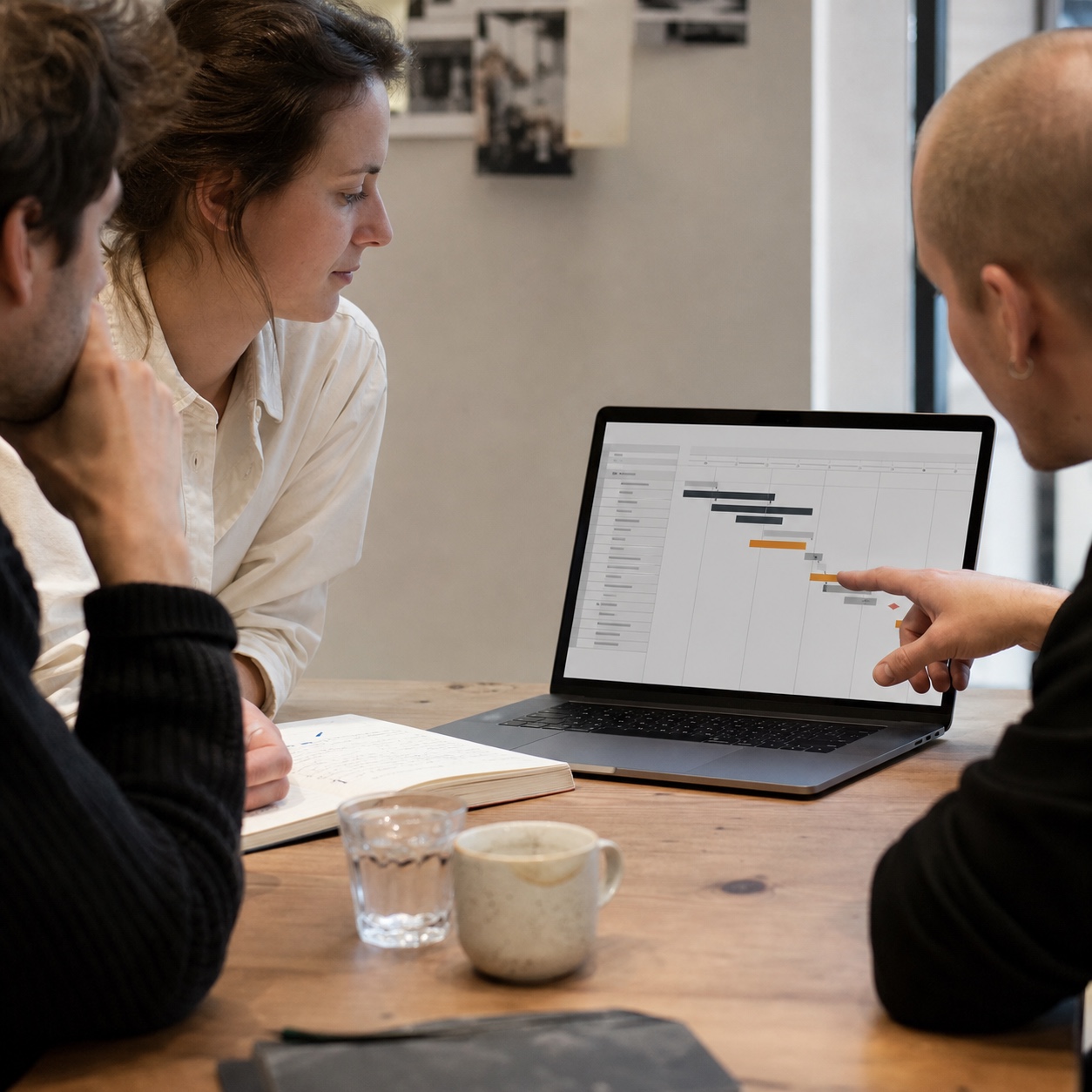 Team reviewing a flagged construction schedule risk Small project team gathered around a laptop reviewing a flagged construction schedule risk item. | Sky Rye Design Small project team gathered around a laptop reviewing a flagged construction schedule risk item.