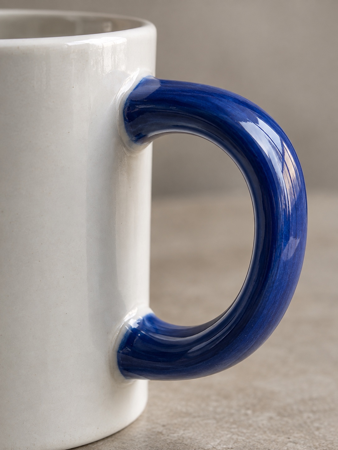 Macro detail of a cobalt blue handle attached to a white ceramic mug body