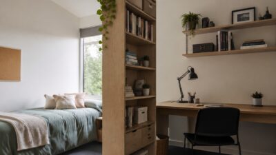 Compact dorm room with a separated bed, desk, and bookshelf divider.