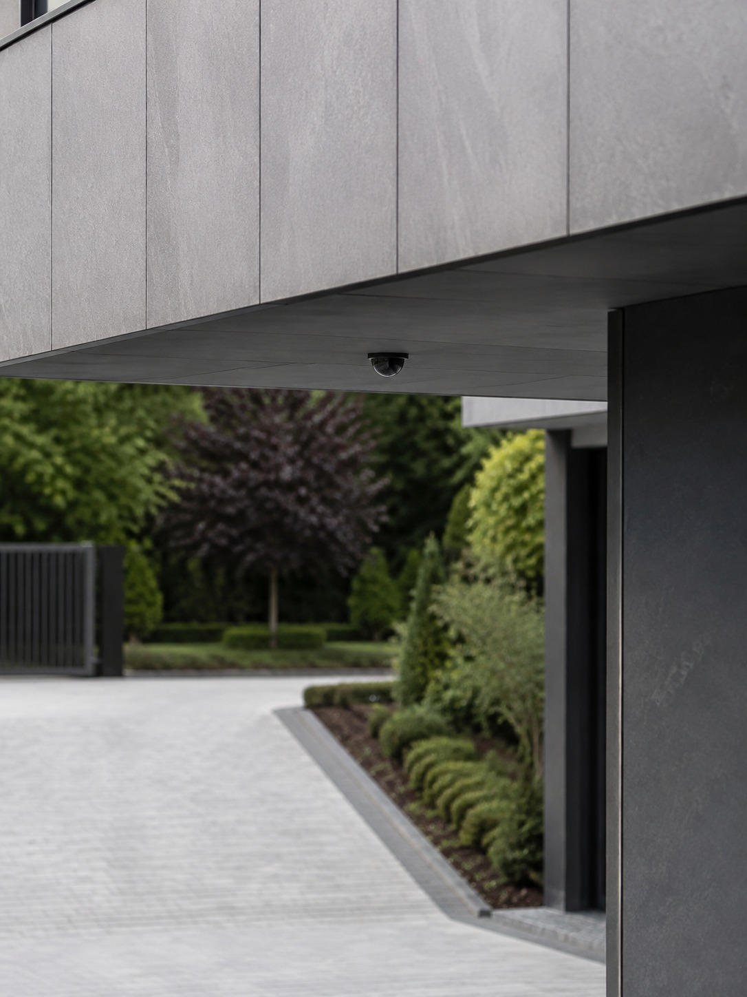 Discreet eave security camera Security camera mounted under a gray overhang of a modern building, overlooking a paved driveway and trimmed shrubs in the background. | Sky Rye Design A discreet security camera mounted under a modern eave with a clear view toward the driveway and gate.