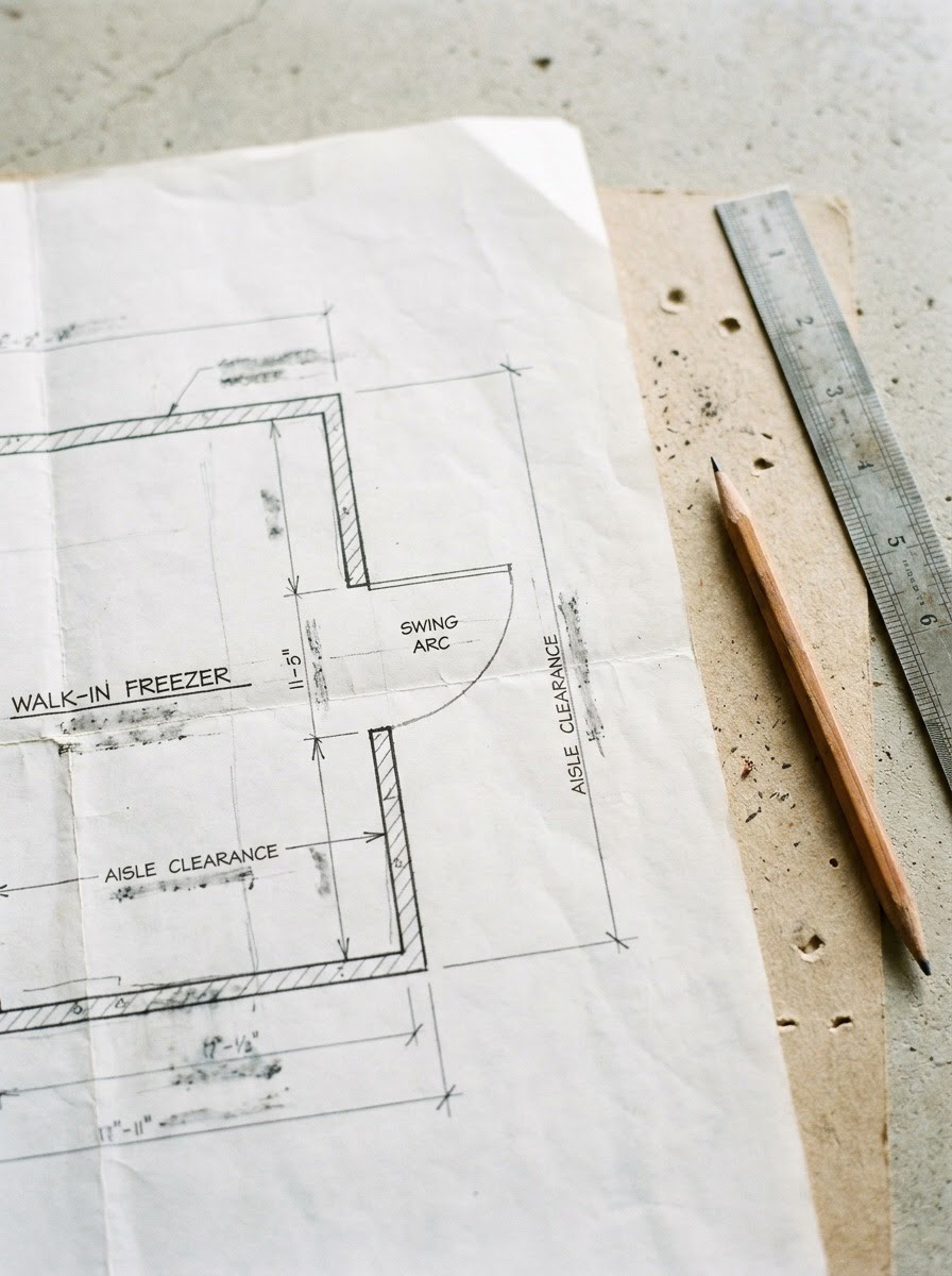 Walk-In Freezer Door Swing Blueprint Architectural floor plan on wrinkled blueprint with a pencil and ruler nearby, showing aisle clearance and a swing‑arc door for a walk‑in freezer area. | Sky Rye Design Blueprint showing a walk-in freezer door swing and aisle clearance lines