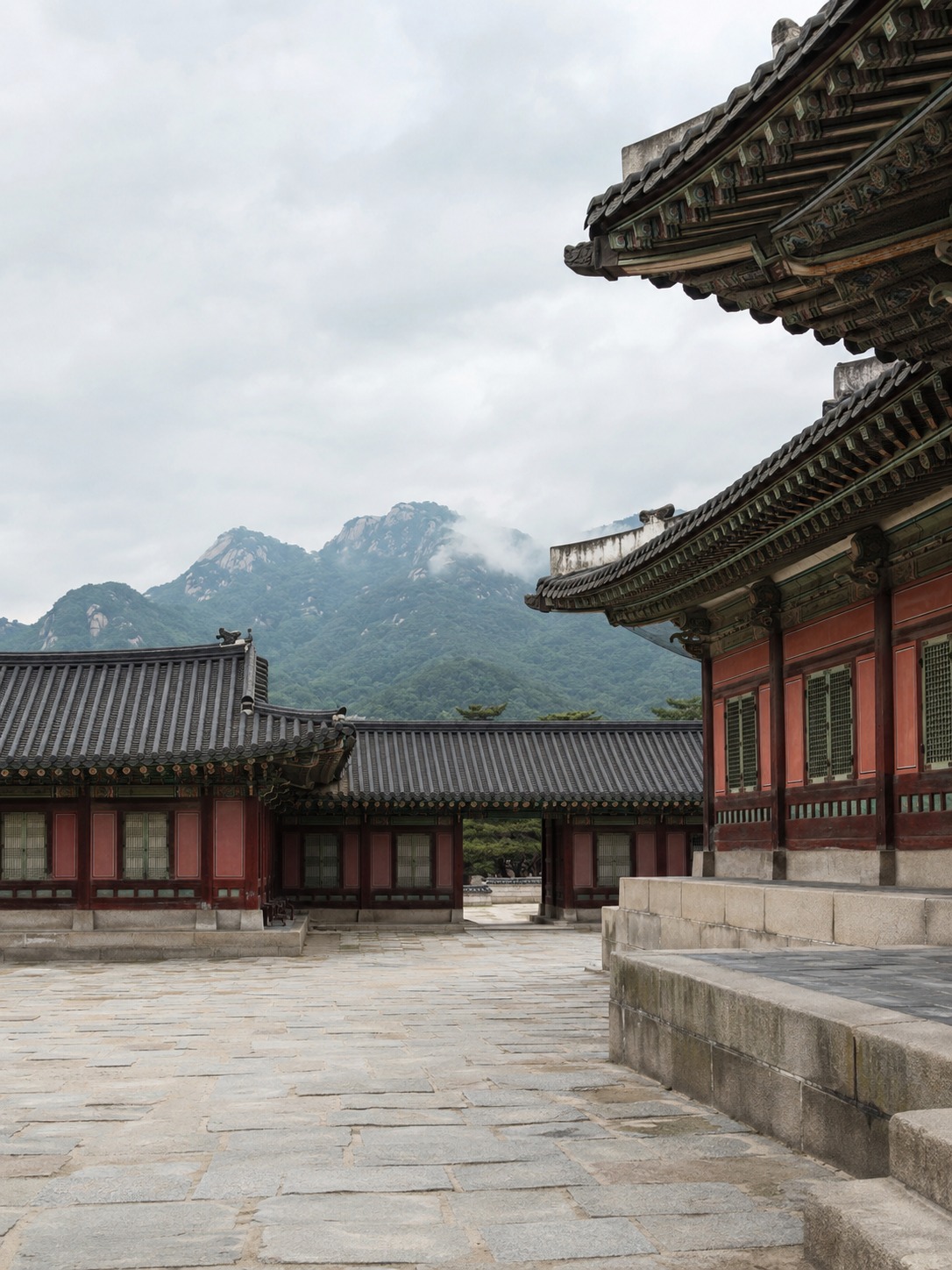 Gyeongbokgung Palace courtyard with modest wooden halls and mountains beyond the walls.