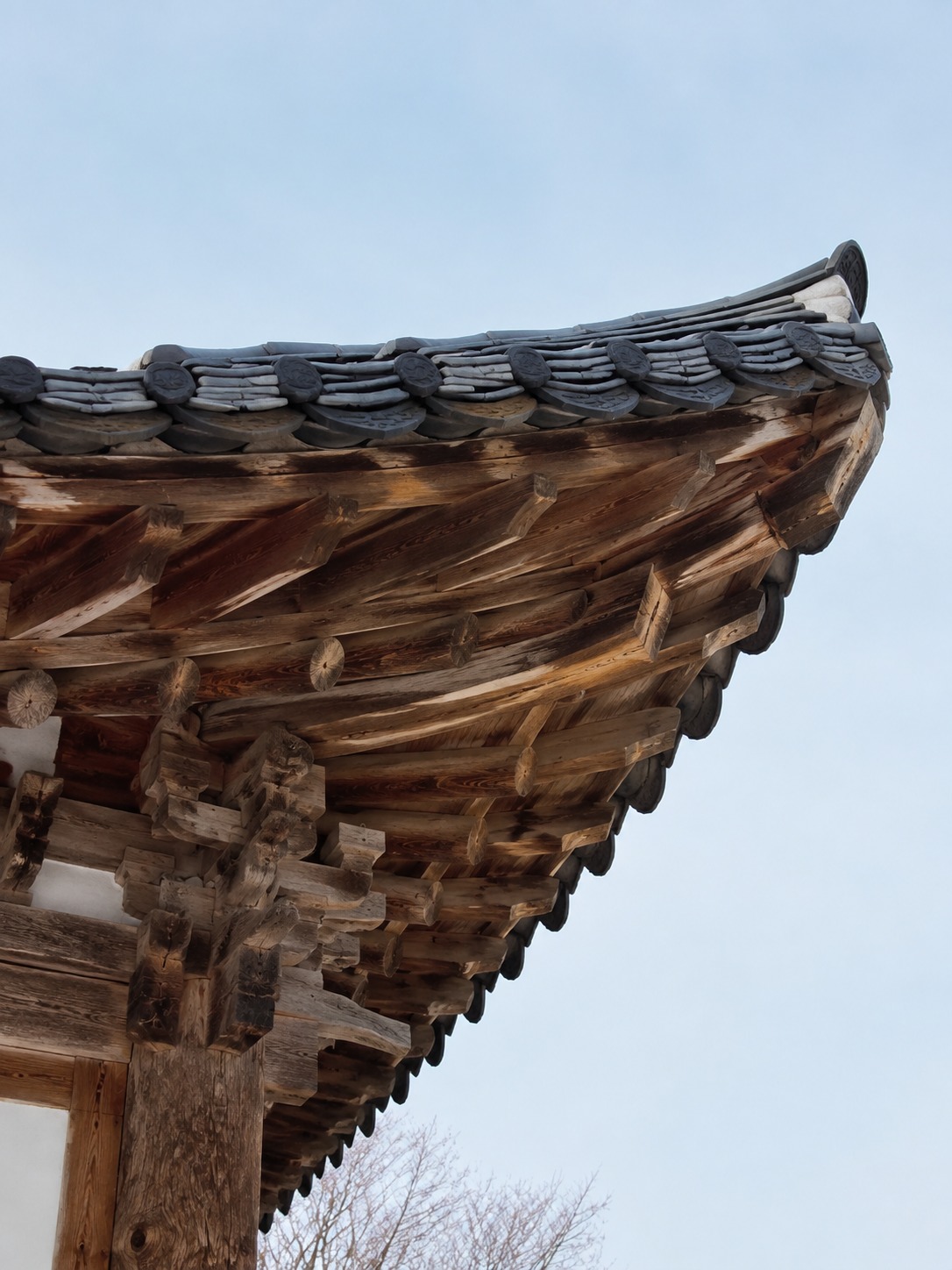 Close view of a hanok cheoma eave showing roof tiles and interlocking timber brackets.