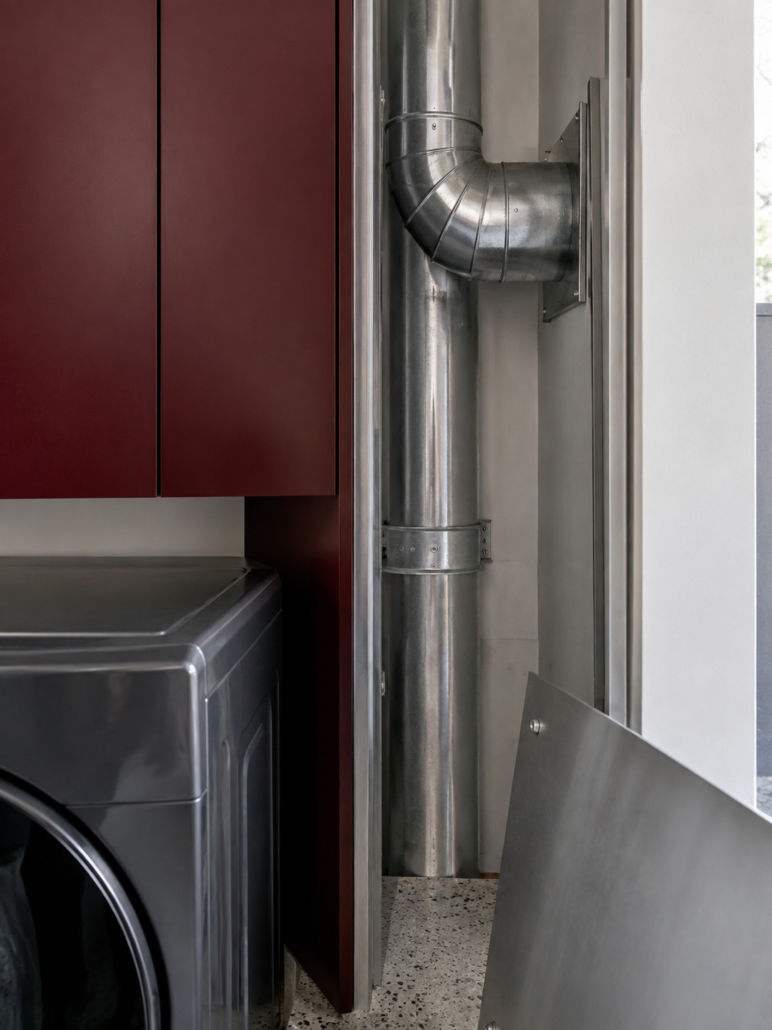 Dryer duct service detail Rigid metal dryer duct in an open service recess beside burgundy cabinetry | Sky Rye Design Rigid metal dryer duct in an open service recess beside burgundy cabinetry