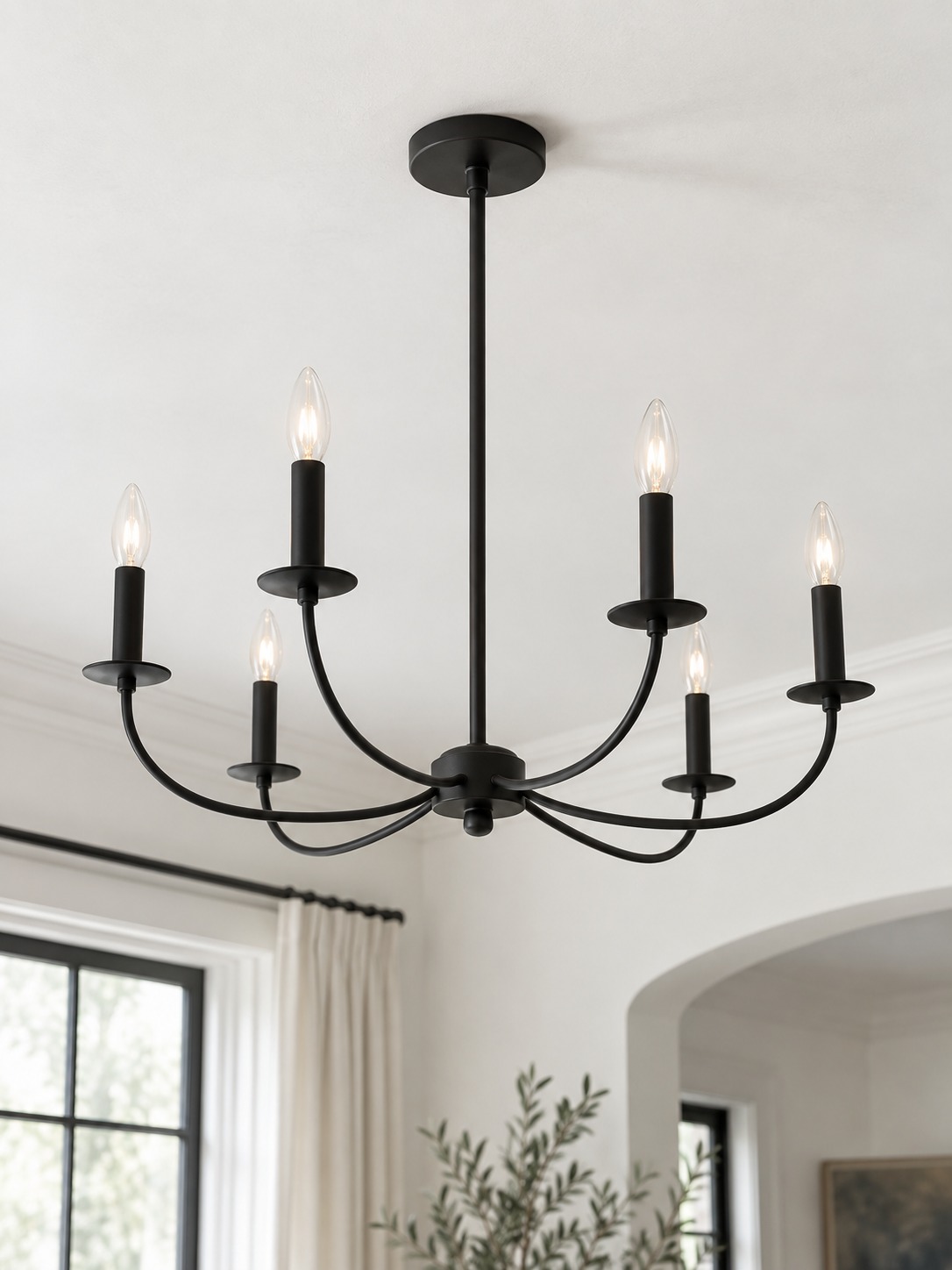 Matte black candle chandelier forming a sharp silhouette against a bright white ceiling