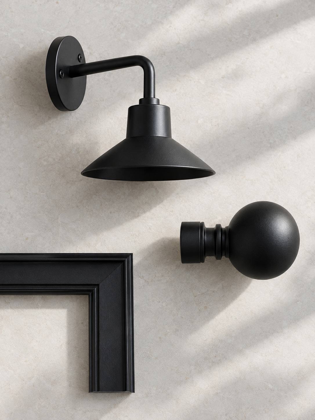 Matte black light bracket curtain rod finial and picture frame corner on a pale surface
