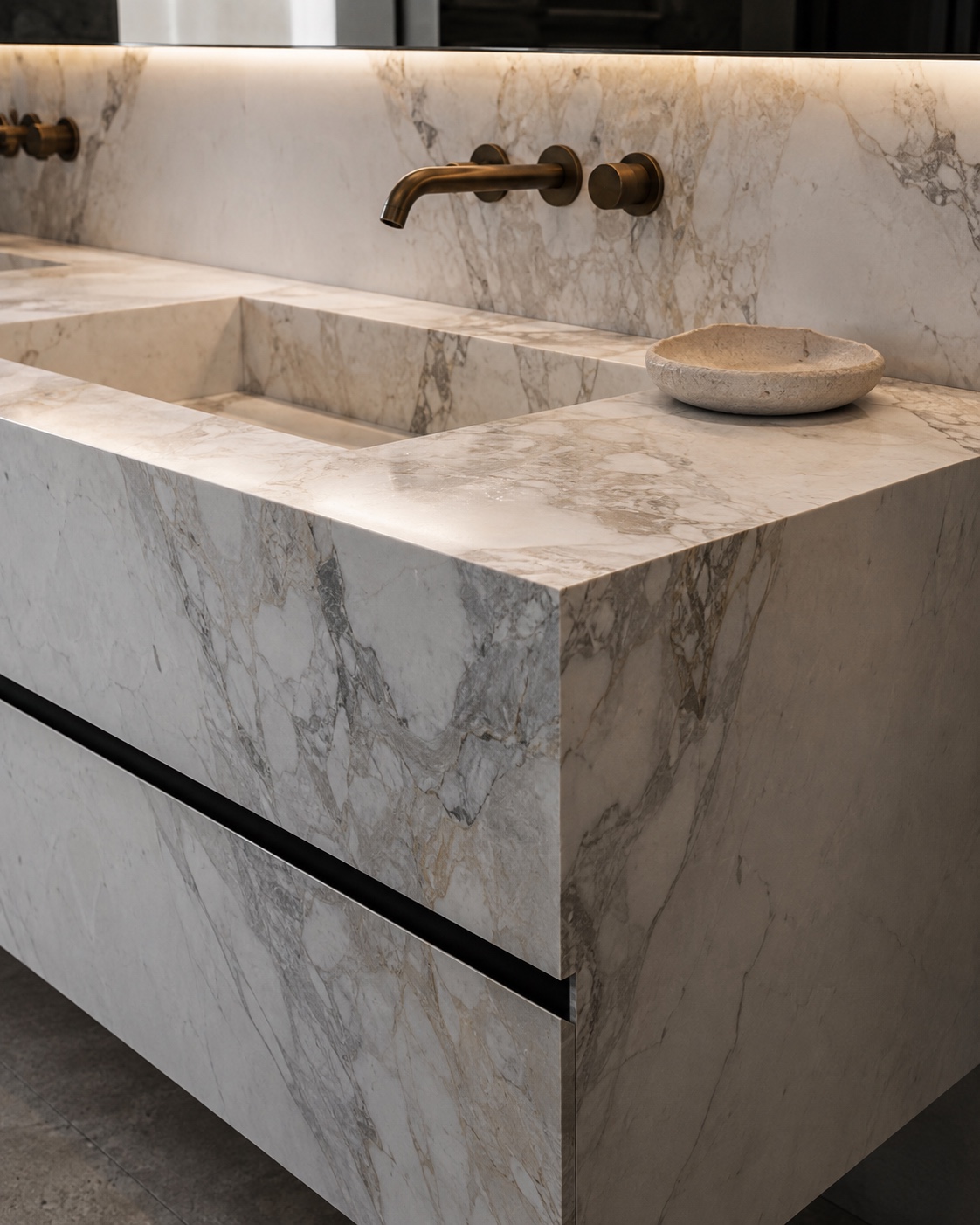 Luxury bathroom vanity detail with monolithic marble sink, brushed brass wall taps and integrated stone countertop