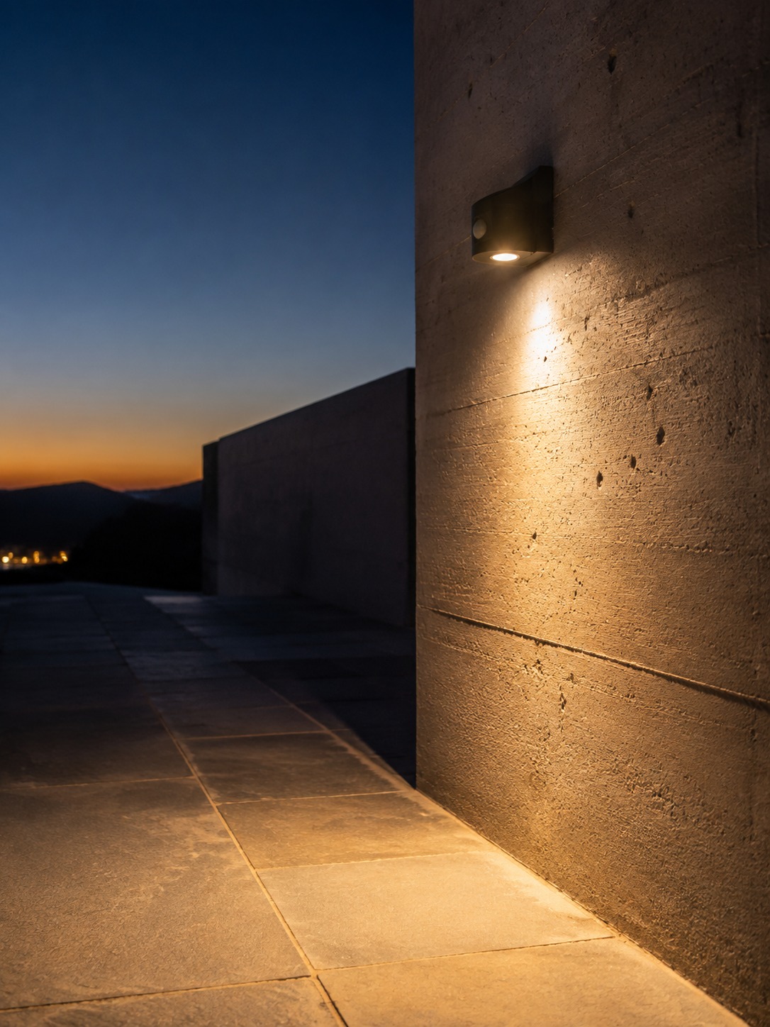 Motion security light on concrete facade A minimalist wall-mounted security light casting warm light onto a stone walkway beside a concrete facade at dusk. | Sky Rye Design A minimalist wall-mounted security light casting warm light onto a stone walkway beside a concrete facade at dusk.