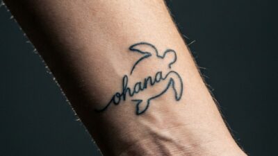 Close inner wrist with fine-line ohana script worked into a honu sea turtle tattoo.