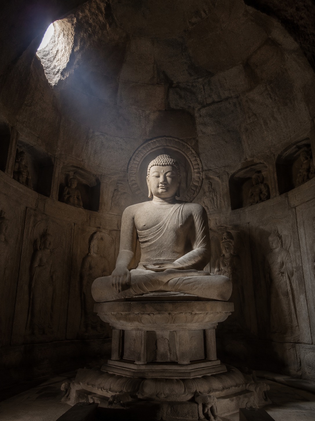 Stone Buddha inside Seokguram Grotto lit by a single beam from the entrance.