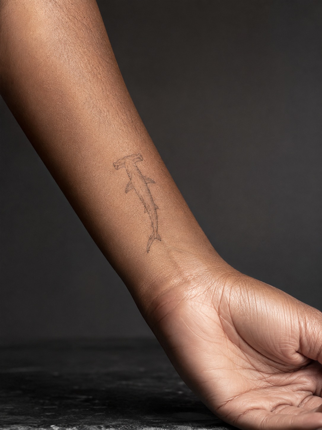 Model showing a fine-line hammerhead shark tattoo on the wrist and lower forearm with realistic healed ink and editorial lighting.