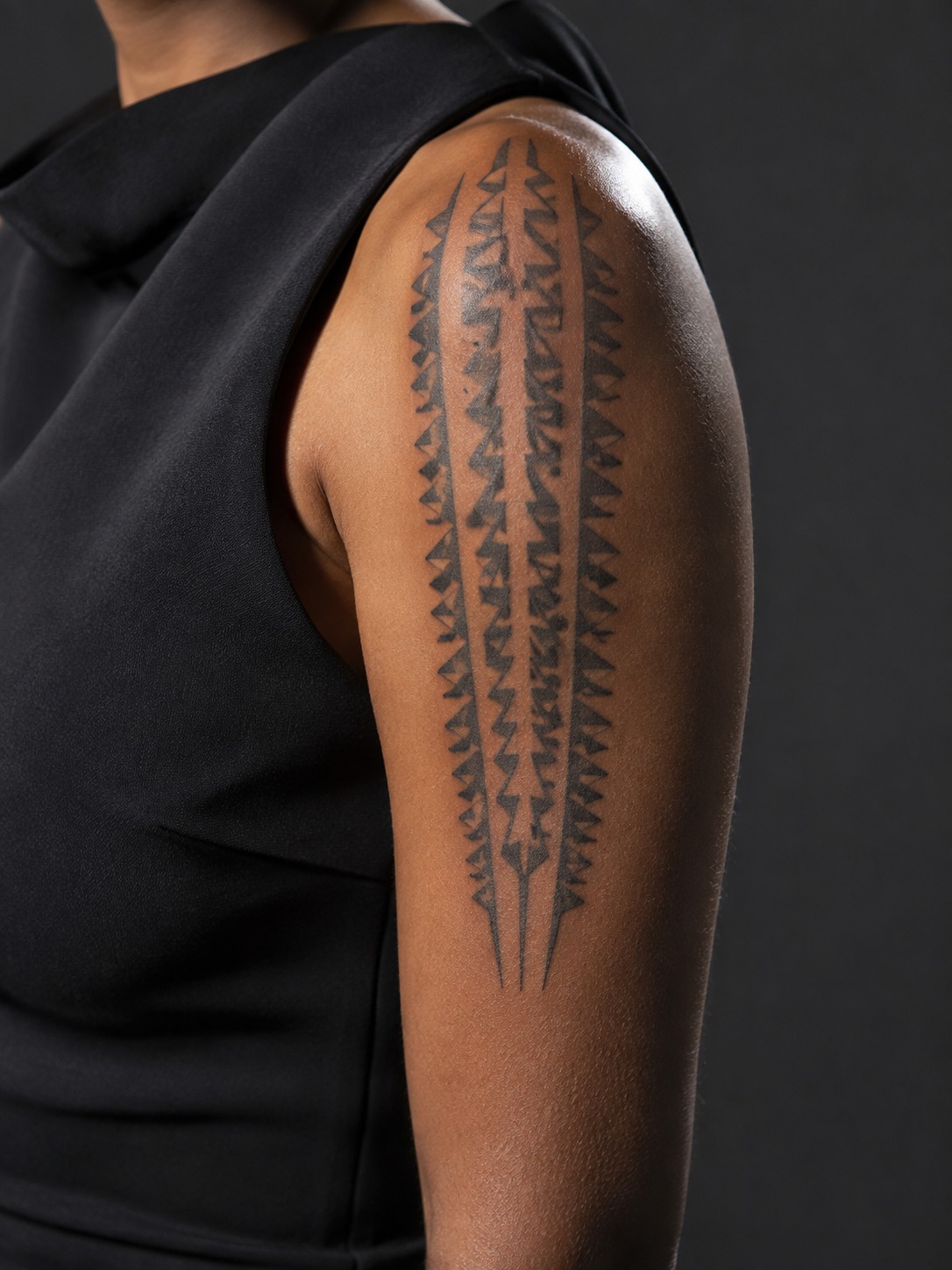Model showing a tribal Polynesian niho mano tattoo on the upper arm and shoulder with realistic healed ink and editorial lighting.