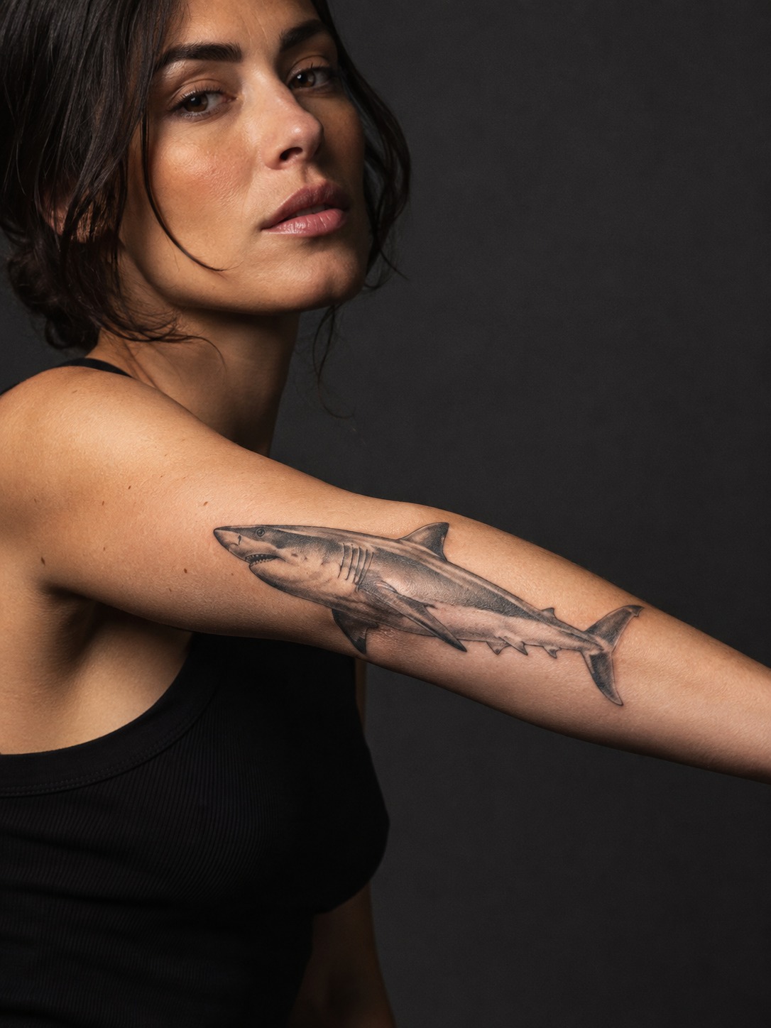 Model showing a realistic mako shark tattoo along the outer forearm with realistic healed ink and editorial lighting.