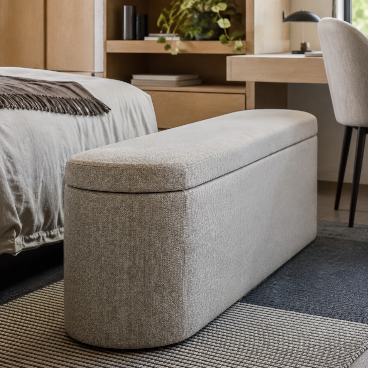 Storage ottoman room divider in a dorm Neutral gray upholstered bench-style ottoman in a tidy bedroom, beside the bed and desk. | Sky Rye Design Neutral storage ottoman creating a soft divider between the bed and desk.