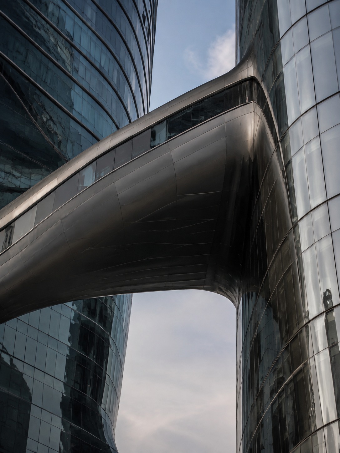 Upward view of The Opus connecting bridge spanning the void between two glass towers.