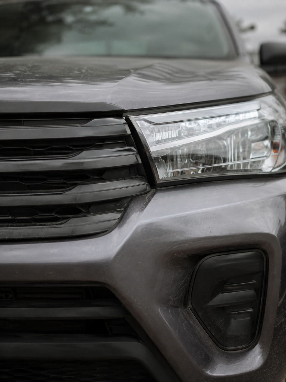 Toyota Hilux grille and headlight detail A close detail of a Toyota Hilux grille and headlight assembly showing plastic and metal surface texture. | Sky Rye Design A close detail of a Toyota Hilux grille and headlight assembly showing plastic and metal surface texture.