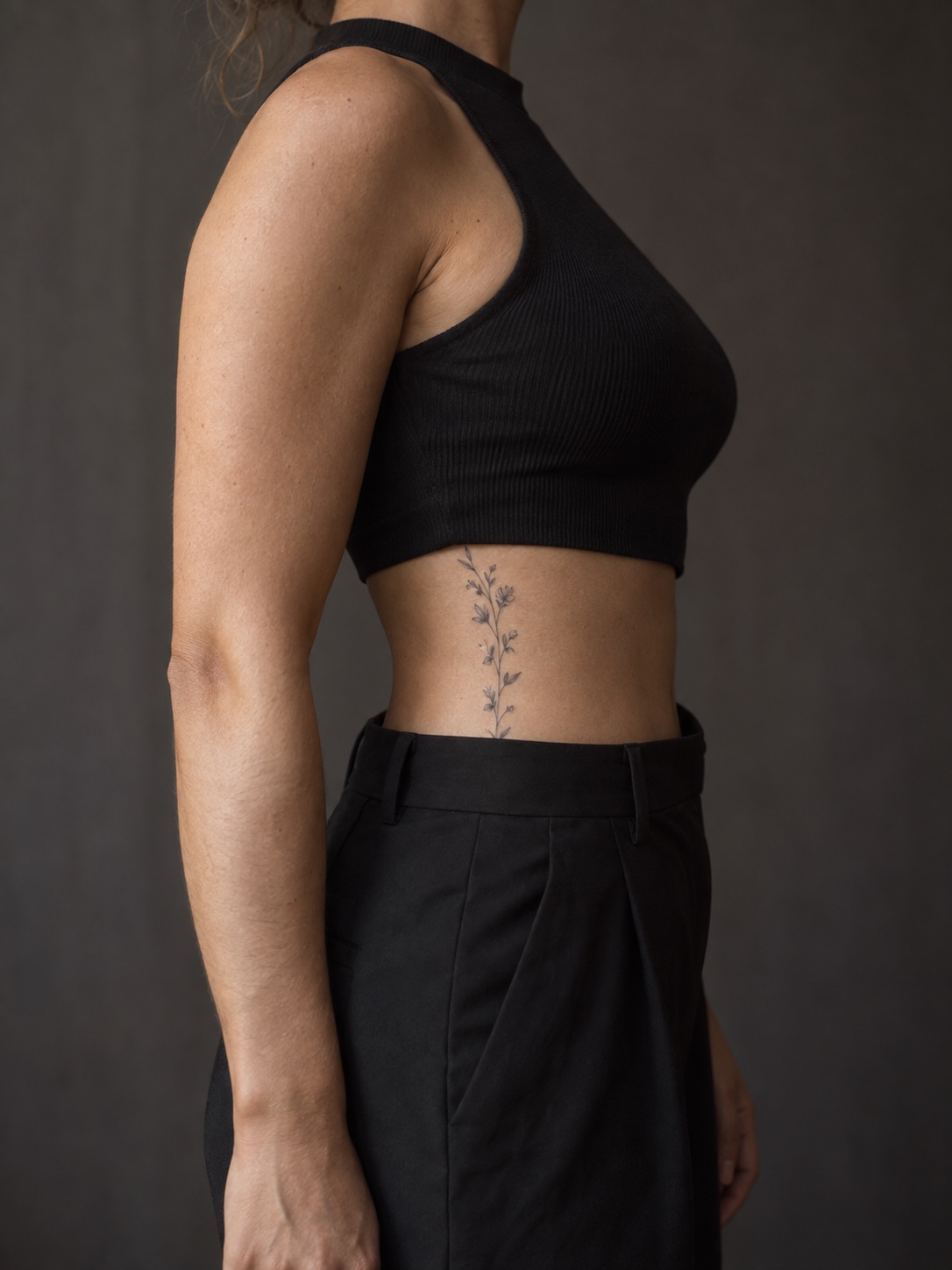 Vertical botanical rib tattoo Vertical botanical fine line tattoo on the side waist between a black top and trousers. | Sky Rye Design Vertical botanical fine line tattoo on the side waist between a black top and trousers.