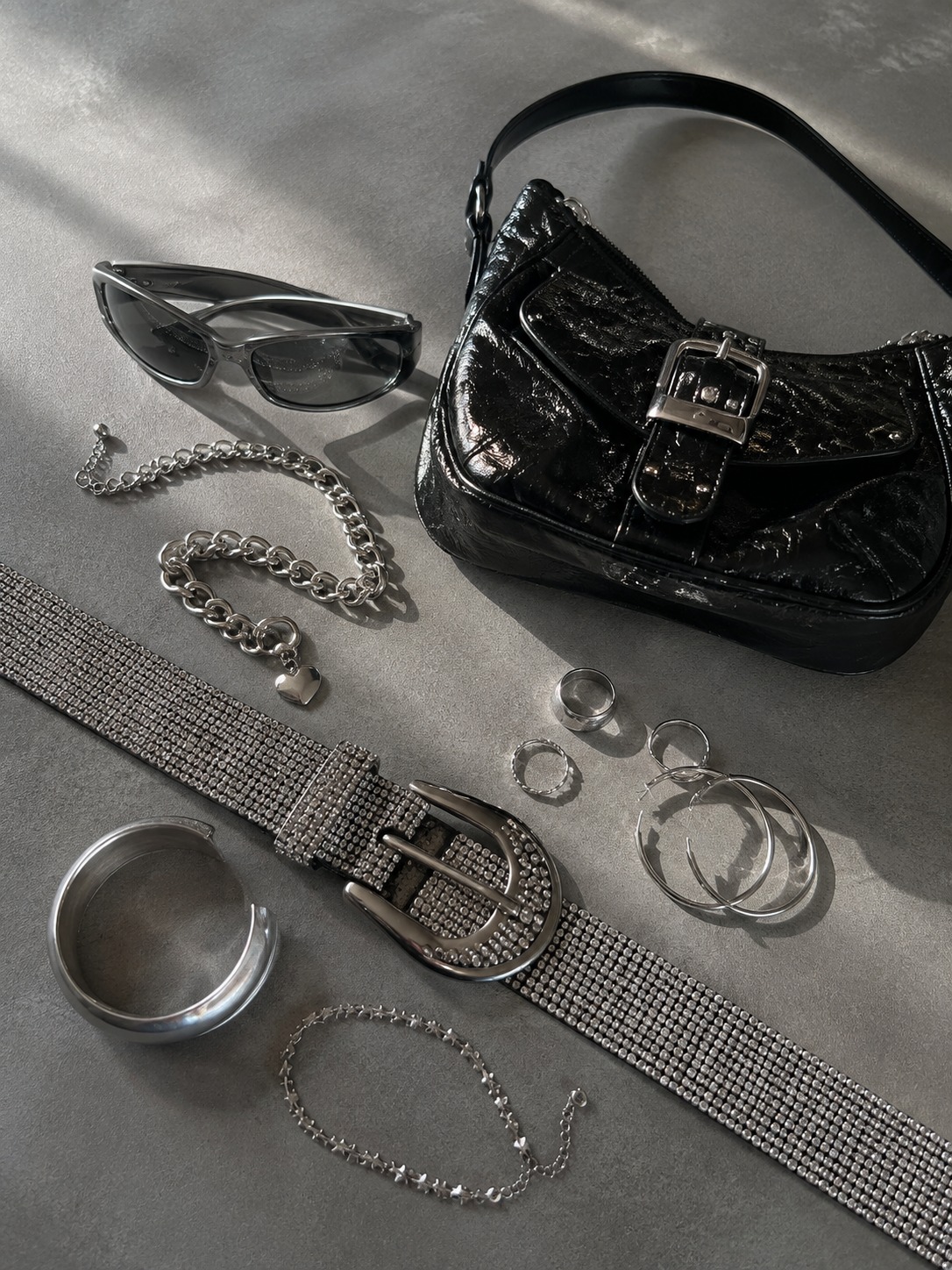 Balanced accessories flat lay Rhinestone belt, chrome jewelry, tinted sunglasses and glossy mini bag | Sky Rye Design Rhinestone belt, chrome jewelry, tinted sunglasses and glossy mini bag