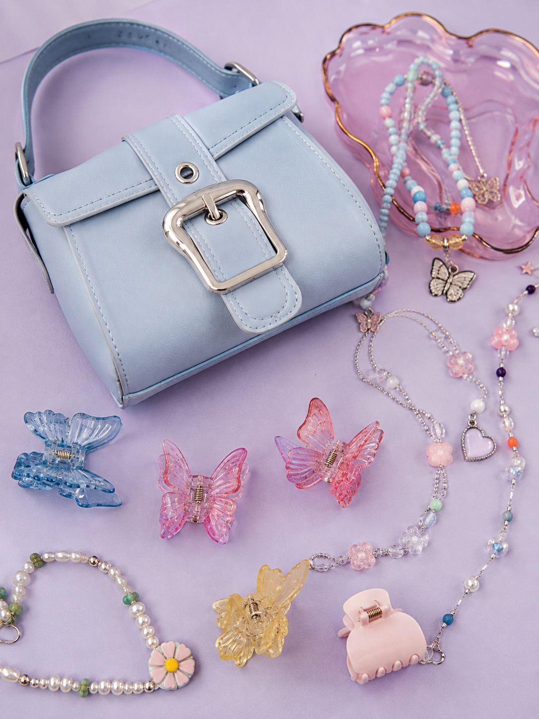 Pastel accessories flat lay Baby blue mini bag, butterfly clips and pastel jewelry on lavender | Sky Rye Design Baby blue mini bag, butterfly clips and pastel jewelry on lavender