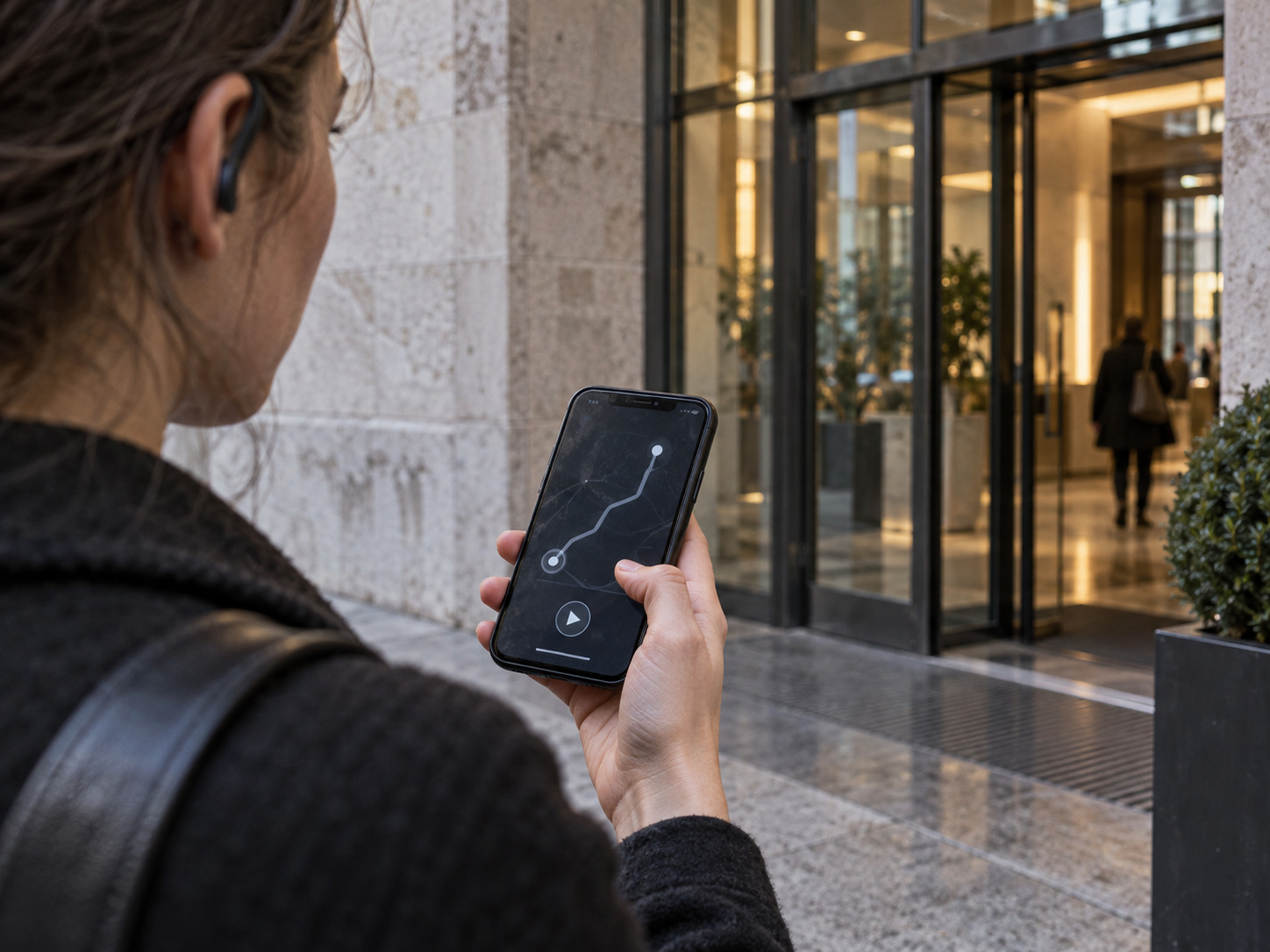 Visitor using an audio guide beside a limestone and glass entrance