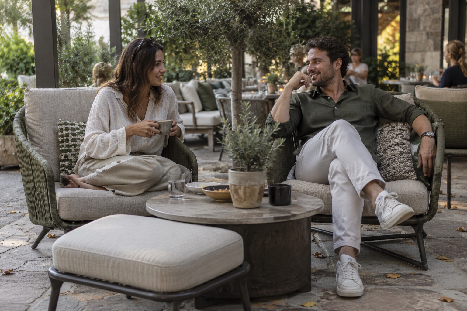 Two guests relaxing in cushioned outdoor lounge chairs at a café patio.