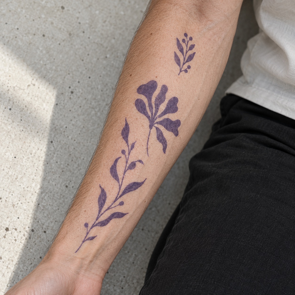 Three purple botanical stencil designs in different sizes on a forearm