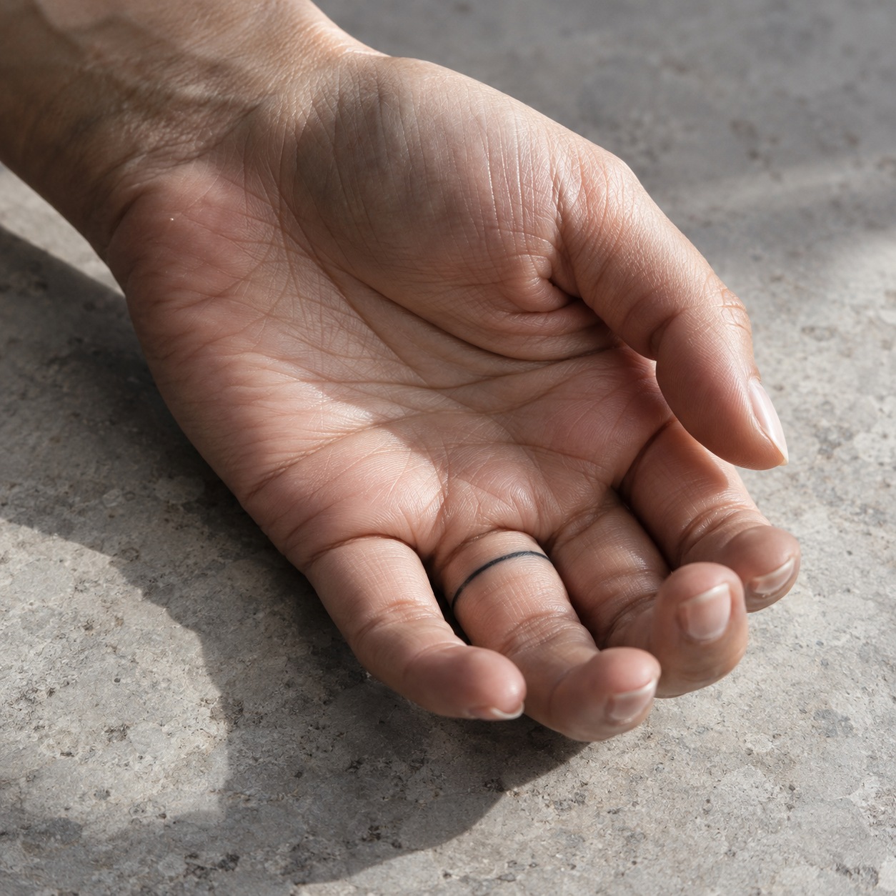 Palm-up hand showing a slim black line tattoo inside the ring finger