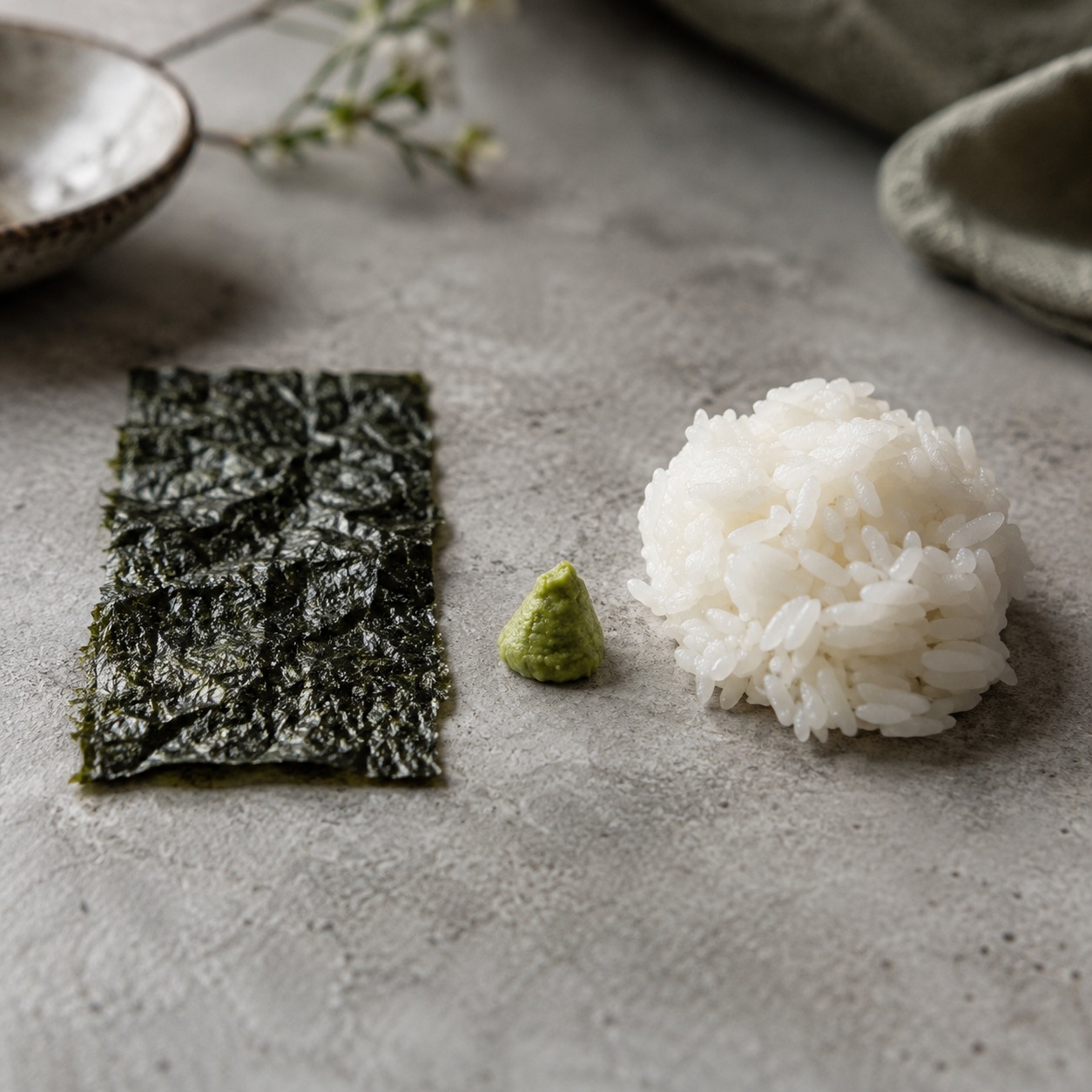 Macro comparison of crinkled nori, soft sushi rice and a small mound of wasabi